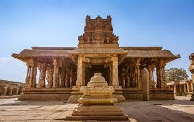 Ancient stone temple in Hampi, India, featuring intricately carved pillars and a grand entrance under a clear blue sky, showcasing the architectural splendor of the Vijayanagara Empire