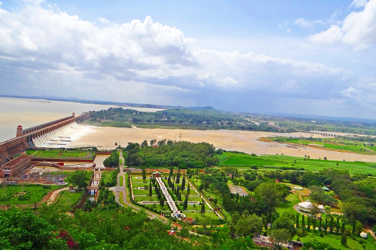 A scenic view of the Tungabhadra Dam with flowing water, lush gardens, and a cloudy sky.