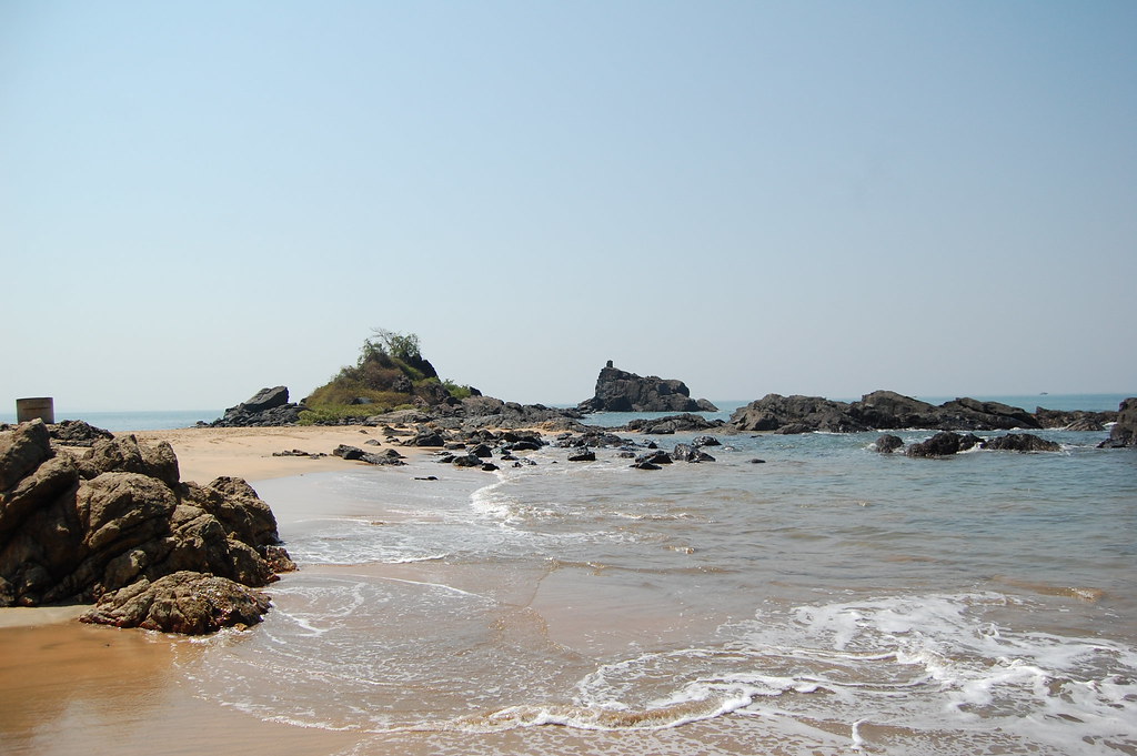 A serene beach in Gokarna with golden sand, rocky formations, and gentle ocean waves under a clear blue sky.